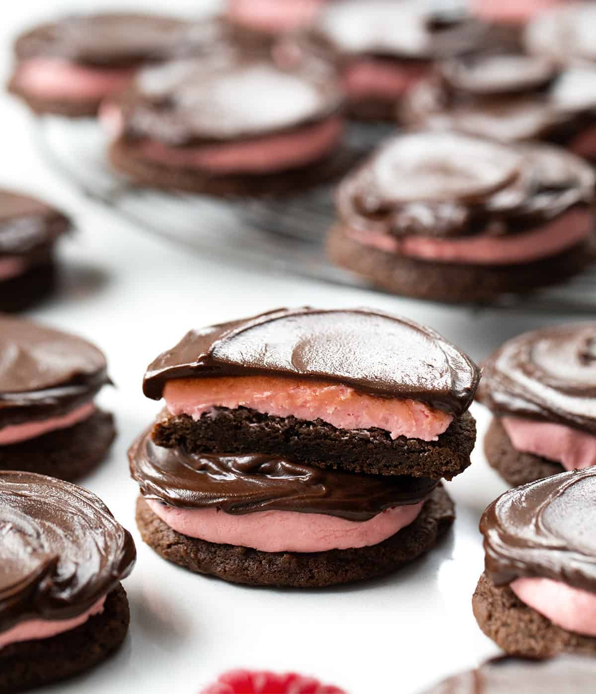 Soft, chocolatey cookies topped with a sweet and tangy raspberry buttercream and finished with a shiny chocolate ganache. They are rich, chewy, and absolutely delicious! Chocolate Raspberry Cookies with one cookie cut in half.