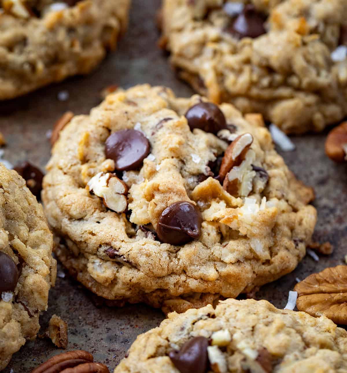 These Cowboy Cookies are thick, chewy, and loaded with oats, chocolate chips, pecans, and coconut. Each bite is soft in the middle with lightly golden edges and a little crunch from the nuts and coconut! Very close up of a Cowboy Cookie showing pecans and coconut and chocolate chips.
