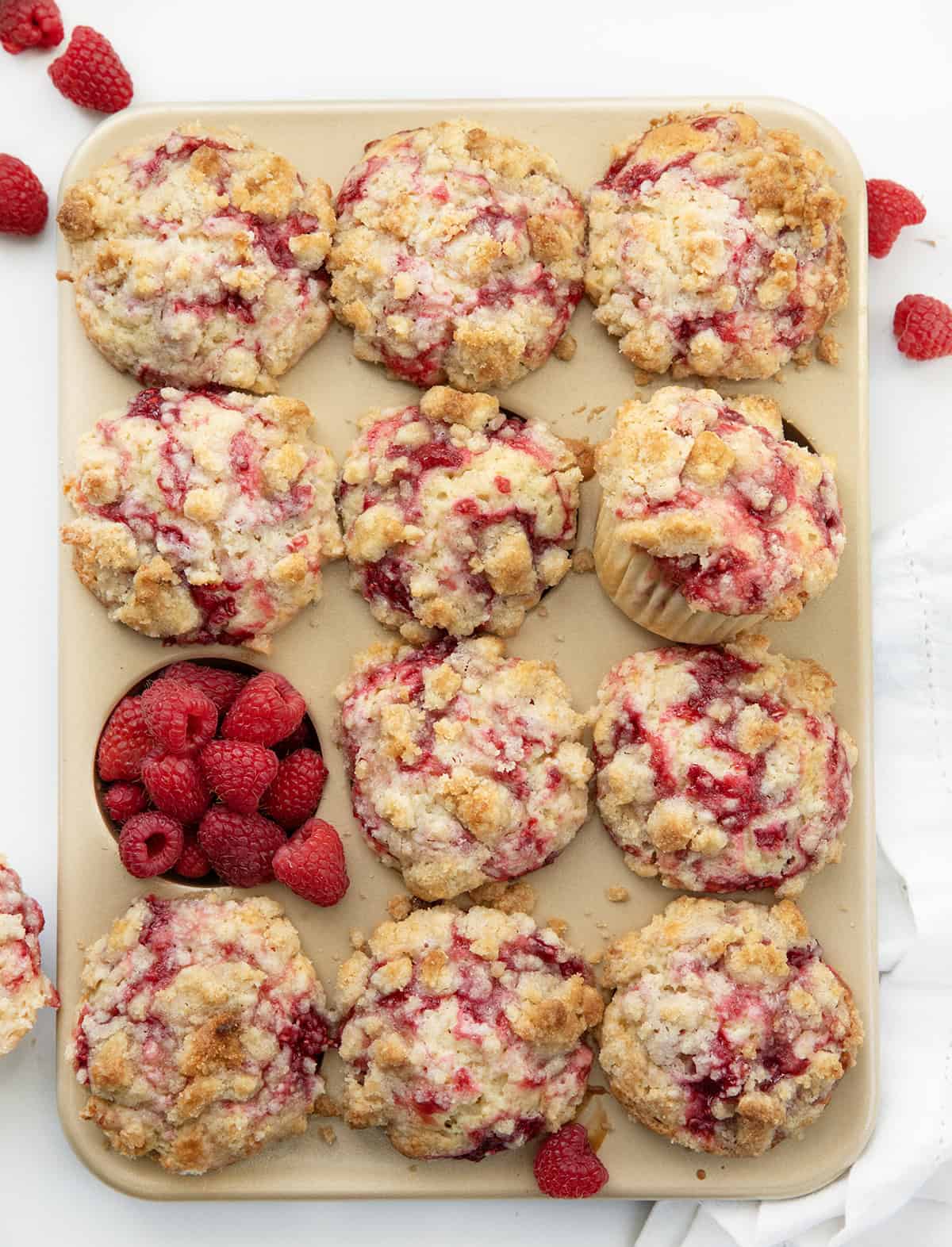 Tray of Double Raspberry Muffins on a white table with fresh raspberries. 