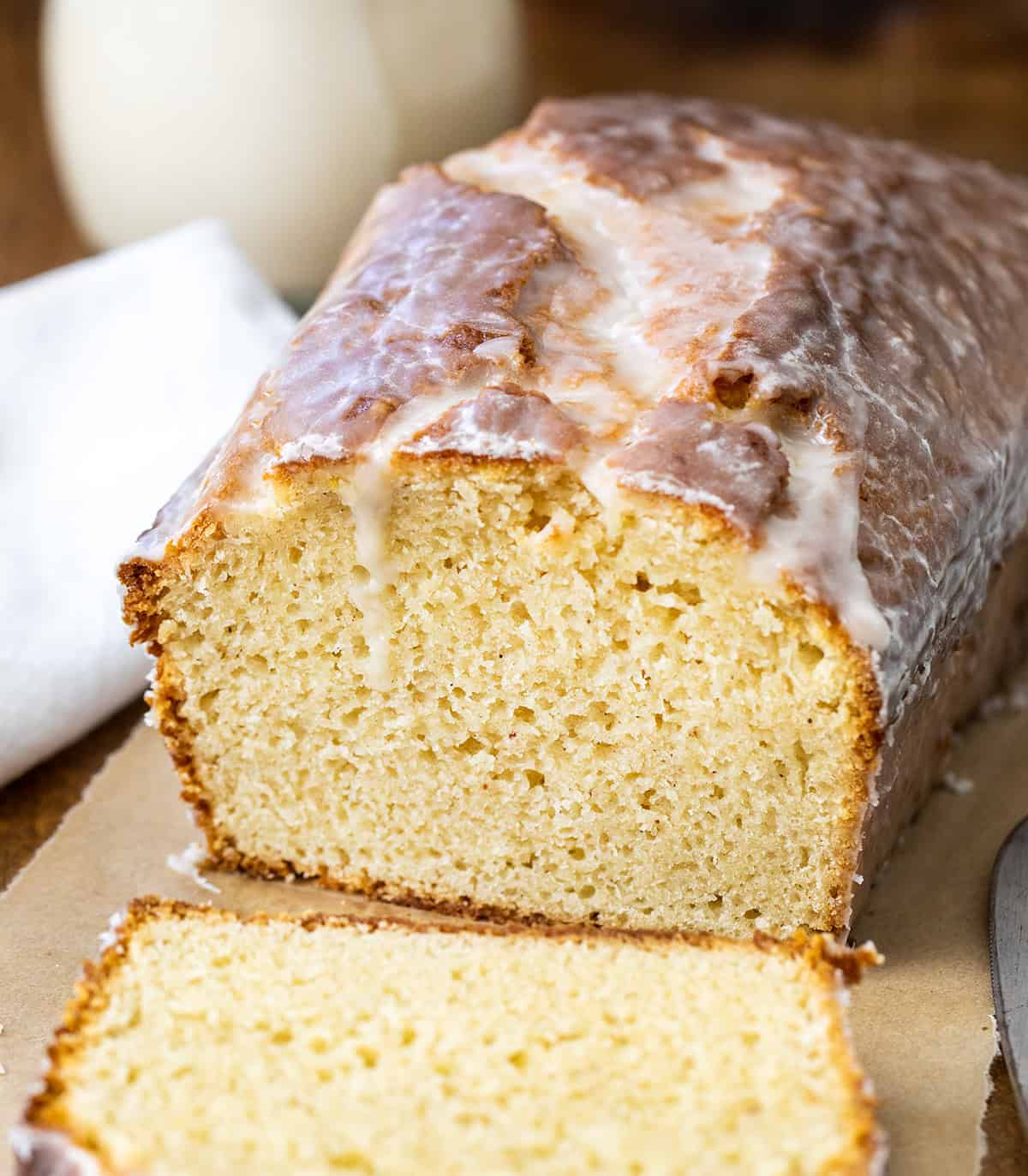 Cut into loaf of Glazed Donut Bread on a wooden table with glaze in background.