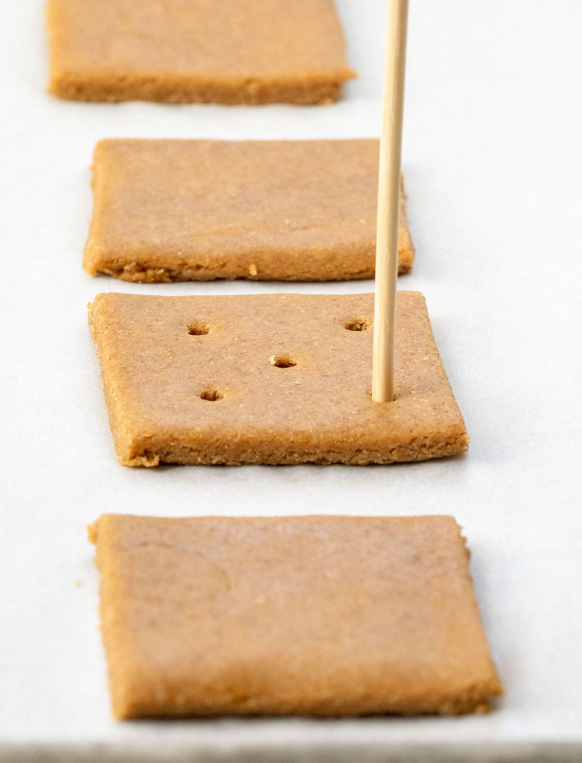 These Homemade Graham Crackers are crisp, slightly sweet, and full of warm cinnamon flavor! Poking holes into Homemade Graham Crackers before being baked.