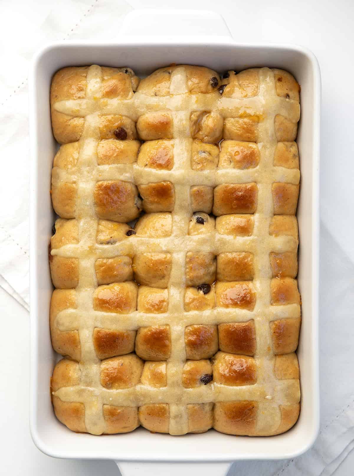 White pan of Hot Cross Buns on a white table from overhead.