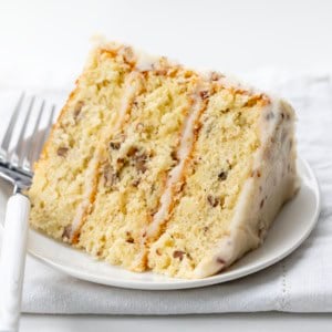 White plate with a piece of Italian Cream Cake on it with a white fork resting on the plate.
