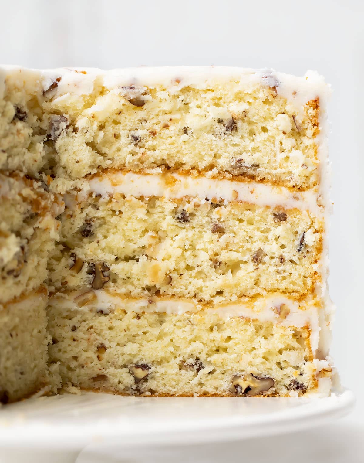 Close up of a Italian Cream Cake on a white cake stand with a portion of the cake removed showing the inside texture.