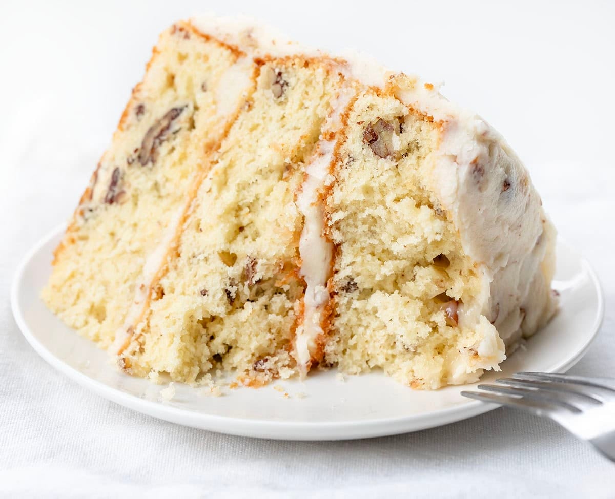 Italian Cream Cake slice on a white plate with a portion of the cake removed from a bite.