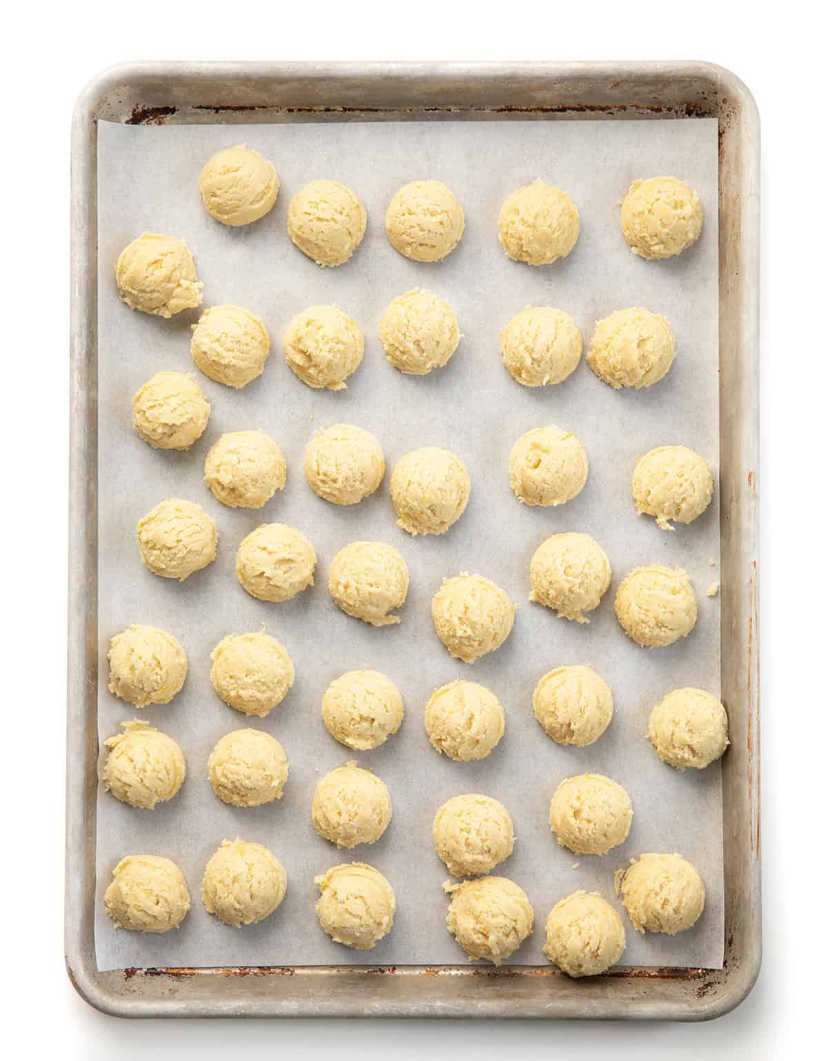 These Lemon Crinkle Cookies are soft, tender, and bursting with bright, fresh lemon flavor. Tray of unbaked and unrolled Lemon Crinkle Cookies on a white table.