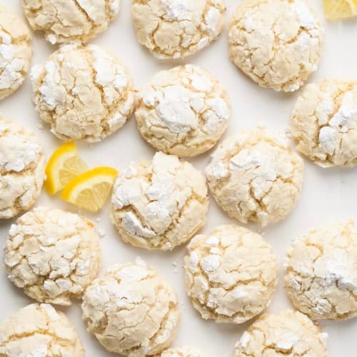 Lemon Crinkle Cookies on a white table with fresh lemon slices.