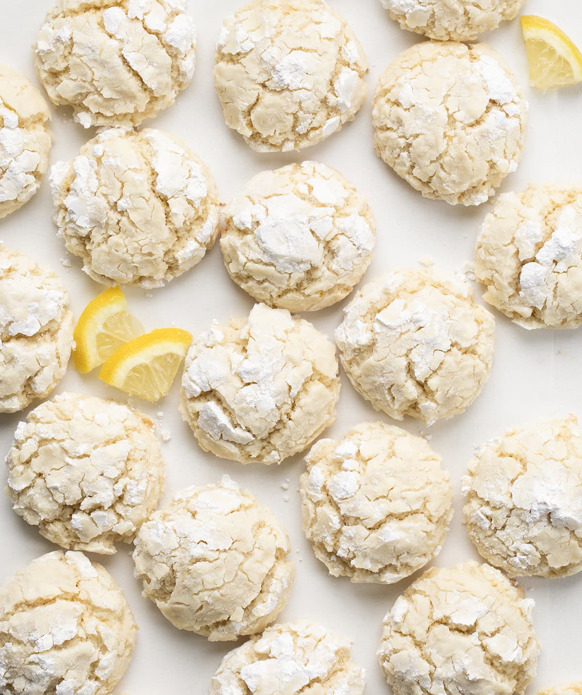 These Lemon Crinkle Cookies are soft, tender, and bursting with bright, fresh lemon flavor. Lemon Crinkle Cookies on a white table with fresh lemon slices.