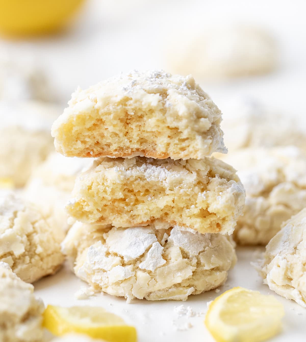 These Lemon Crinkle Cookies are soft, tender, and bursting with bright, fresh lemon flavor. Stack of Lemon Crinkle Cookies on a white table surrounded by more cookies.