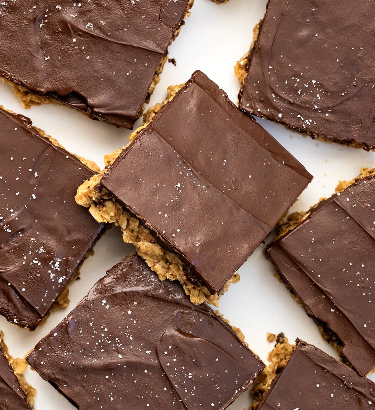 These No-Bake Peanut Butter Oat Bars are a quick, chewy, and chocolate-topped treat you can make with ingredients you probably already have in your pantry! No baking required, just mix, press, and chill! No-Bake Peanut Butter Oat Bars cut into squares and on a white table.