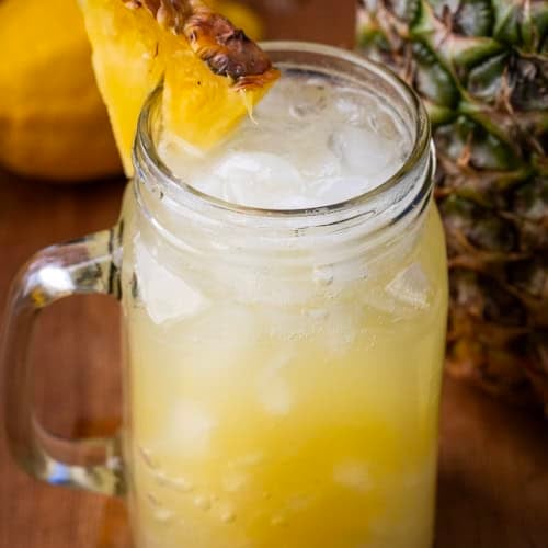 Mason jar of Pineapple Lemonade Punch with a fresh pineapple in the background.