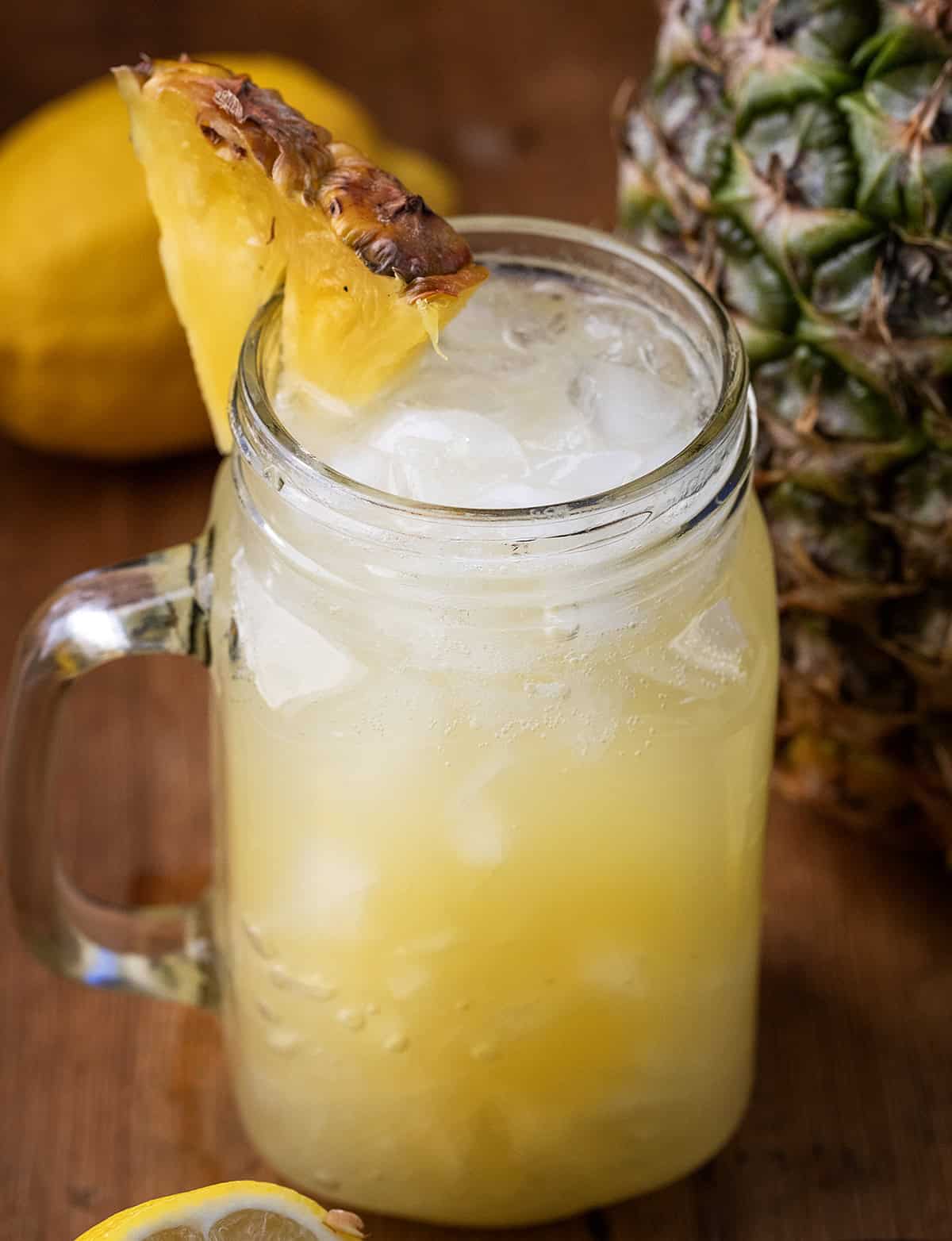 Mason jar of Pineapple Lemonade Punch with a fresh pineapple in the background.