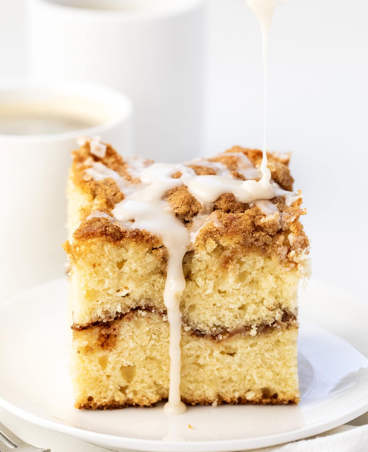 Drizzling glaze over Sour Cream Coffee Cake piece on a white plate.