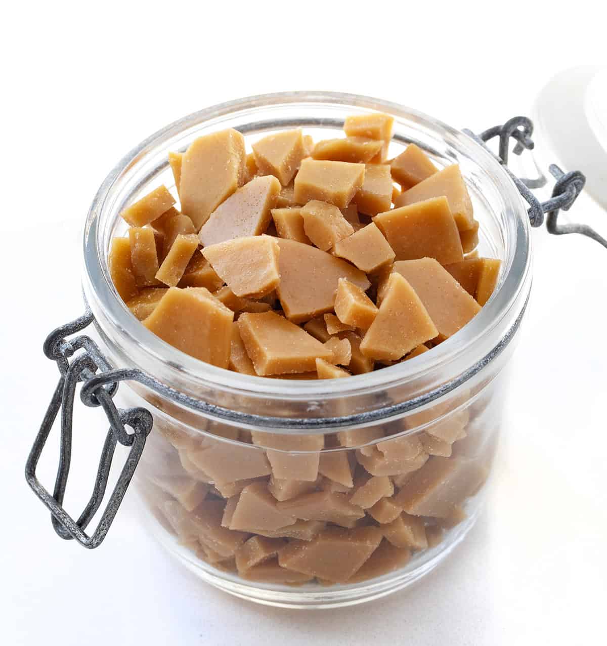 Container filled with Toffee Bits on a white table.