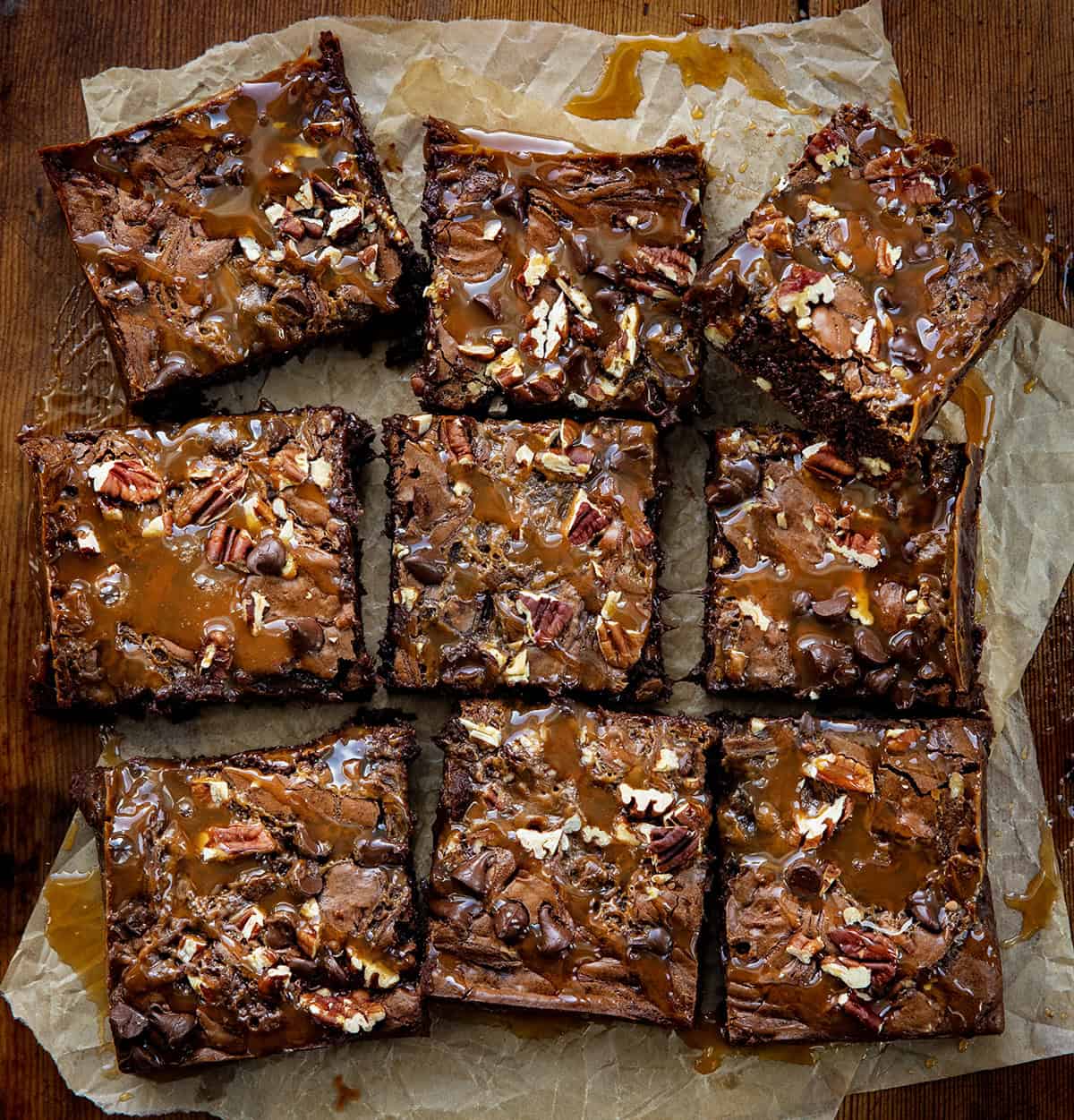Turtle Brownies cut into squares on parchment paper on a wooden table from overhead.