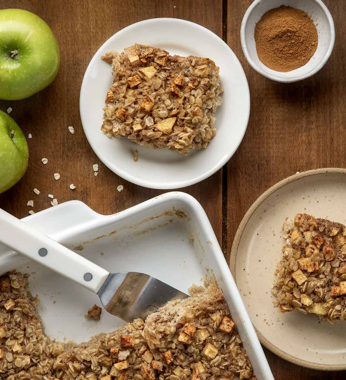 Pieces of Apple Cinnamon Baked Oatmeal on plates next to the pan on a wooden table from overhead.