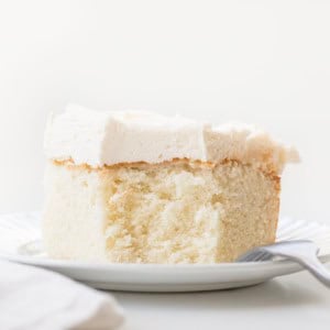 Piece of Best White Sheet Cake on a white plate with a bite removed and a fork resting on the plate.