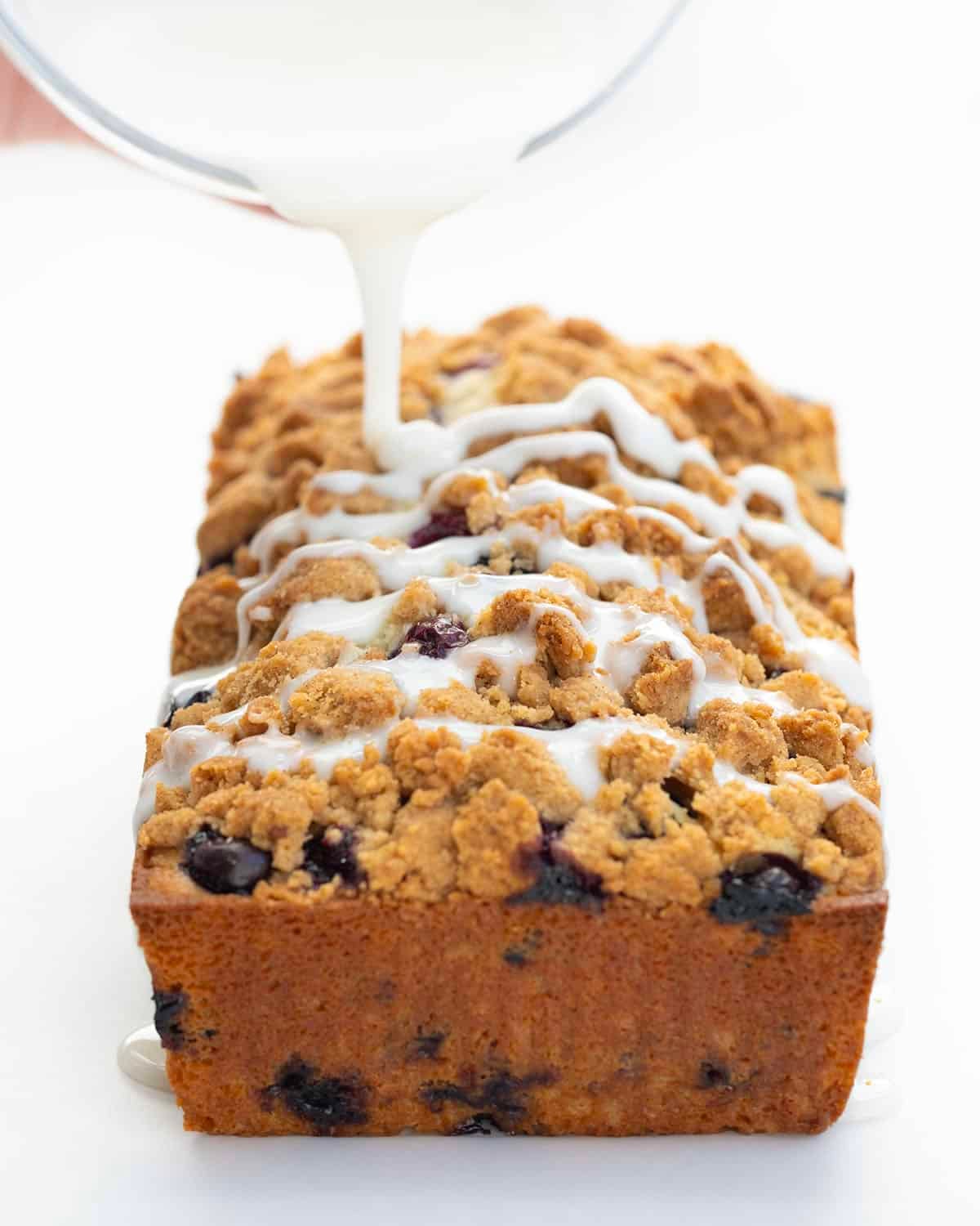 Drizzling vanilla glaze over Blueberry Crumble Bread.