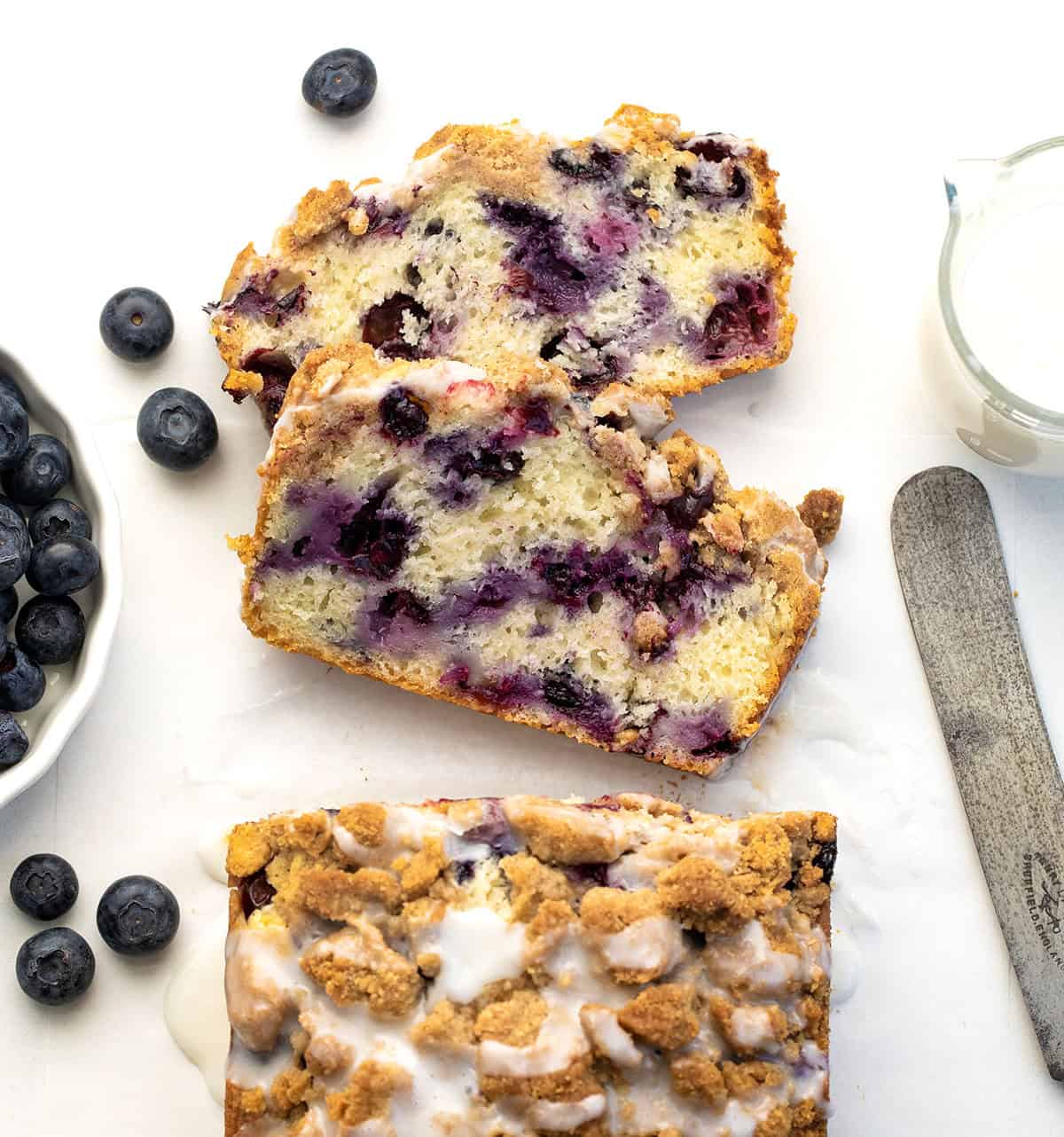 Loaf of Blueberry Crumble Bread with a couple of slices cut and laying flat on a white table.