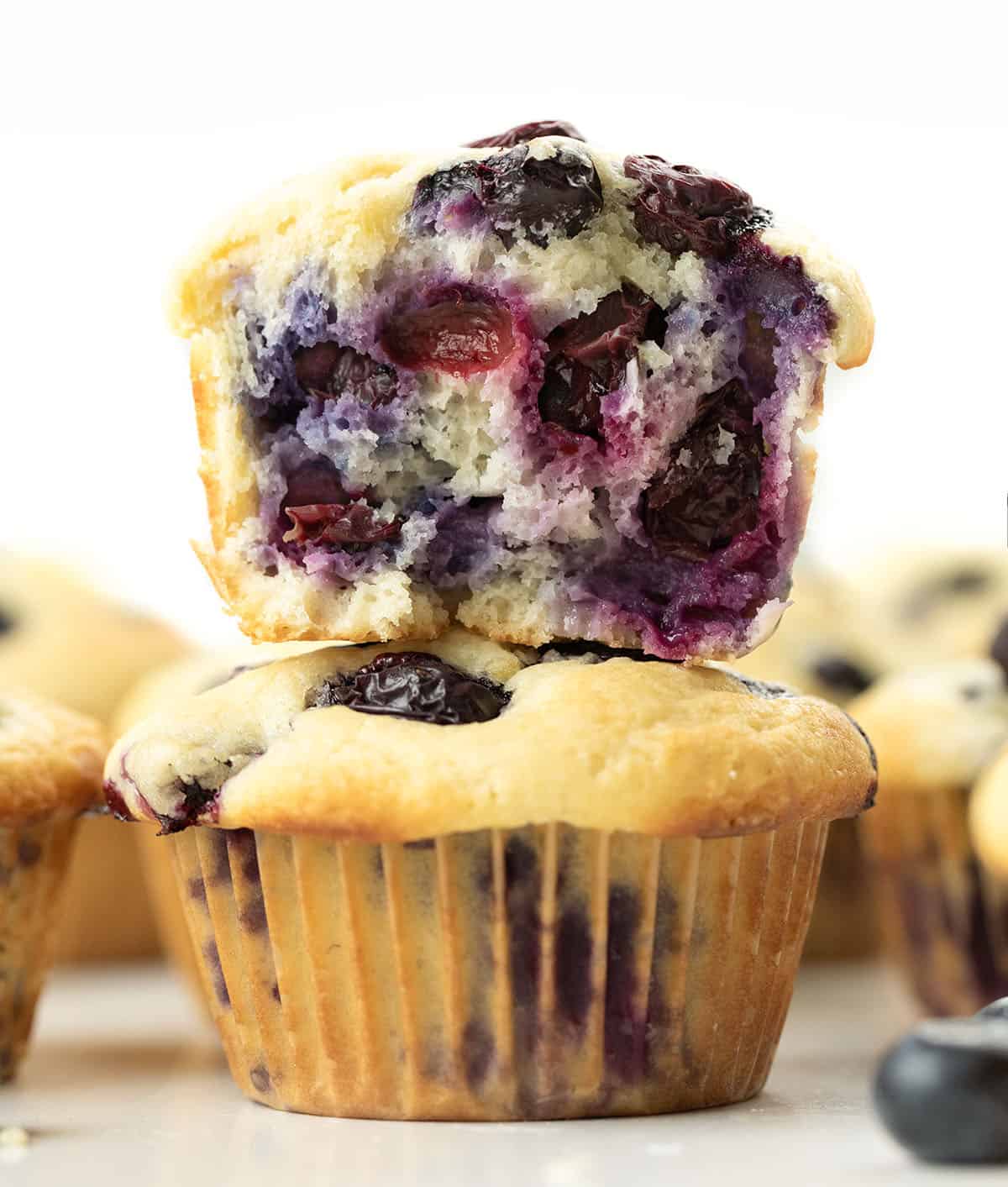 Stacked Blueberry Lemon Muffins and the top muffin is halved showing numerous blueberries inside.