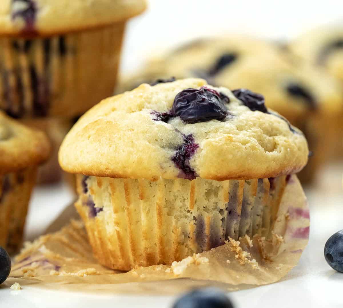 One Blueberry Lemon Muffin with the liner partially removed around other muffins.