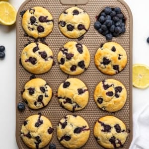 Blueberry Lemon Muffins in the muffin tin with fresh blueberries and lemon from overhead.
