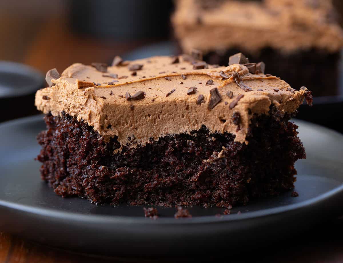 Piece of Chocolate Sheet Cake on a black plate with a bite removed.