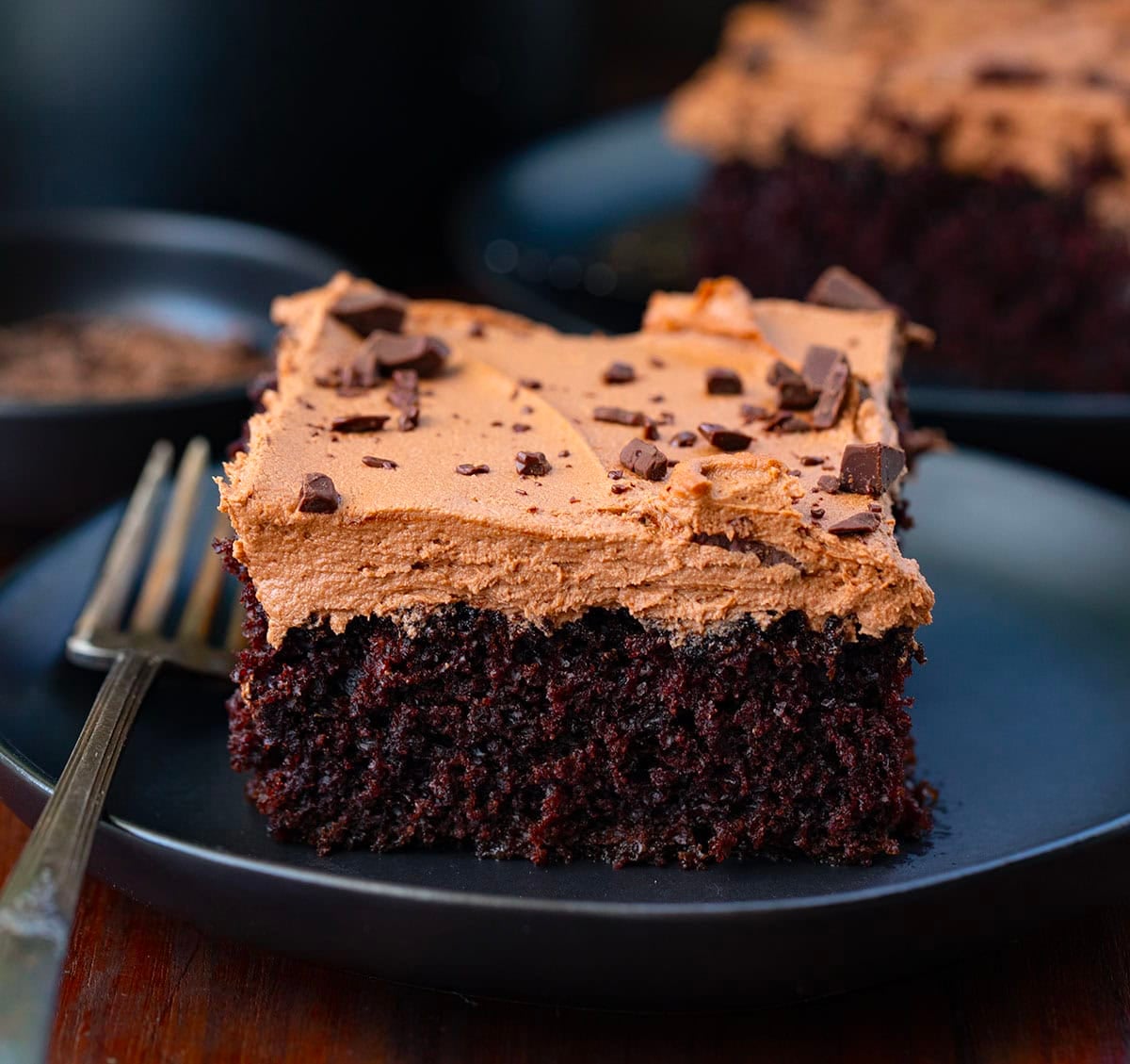 Pieces of Chocolate Sheet Cake on black plates on a wooden table.