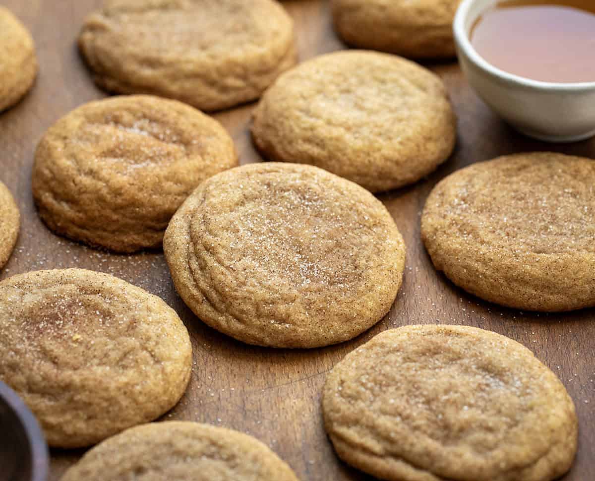 Honey Snickerdoodles laying on a wooden table with a bowl of honey and a bowl of cinnamon sugar.