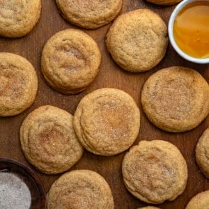 Honey Snickerdoodles laying on a wooden table with a bowl of honey and a bowl of cinnamon sugar from overhead.