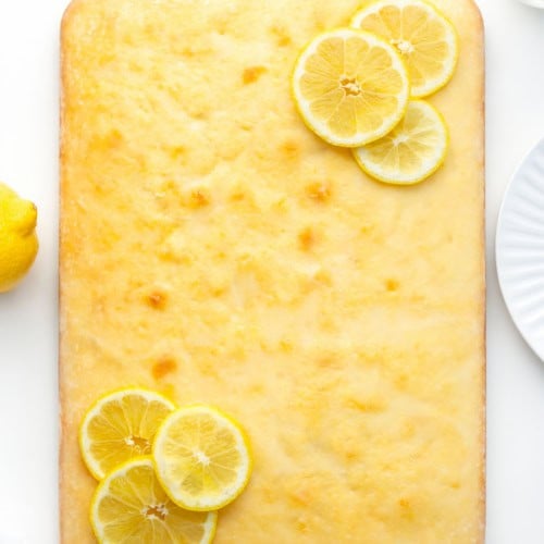 Lemon Sheet Cake on a white table with fresh lemons from overhead.