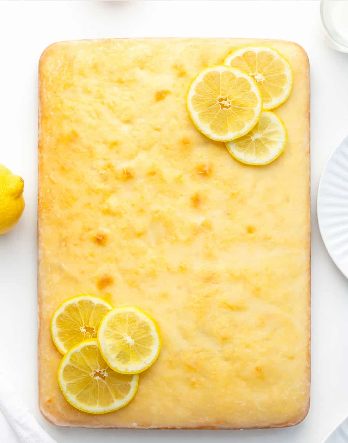 Lemon Sheet Cake on a white table with fresh lemons from overhead. 