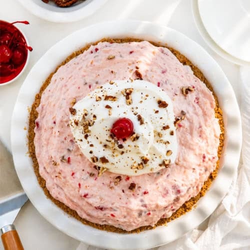 Whole Millionaire Pie on a white table with cherries and pecans from overhead.