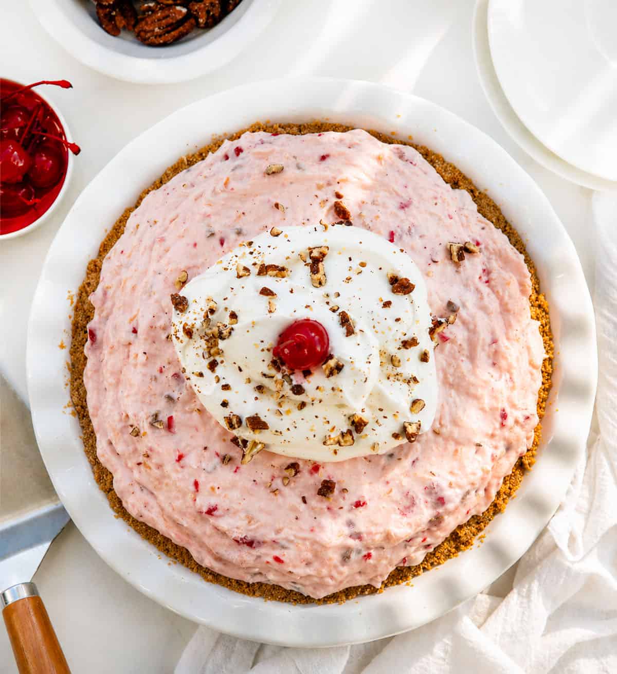 Whole Millionaire Pie on a white table with cherries and pecans from overhead. 