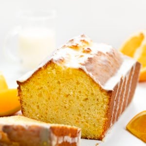 Orange Loaf with some pieces cut away on a white table with fresh oranges.