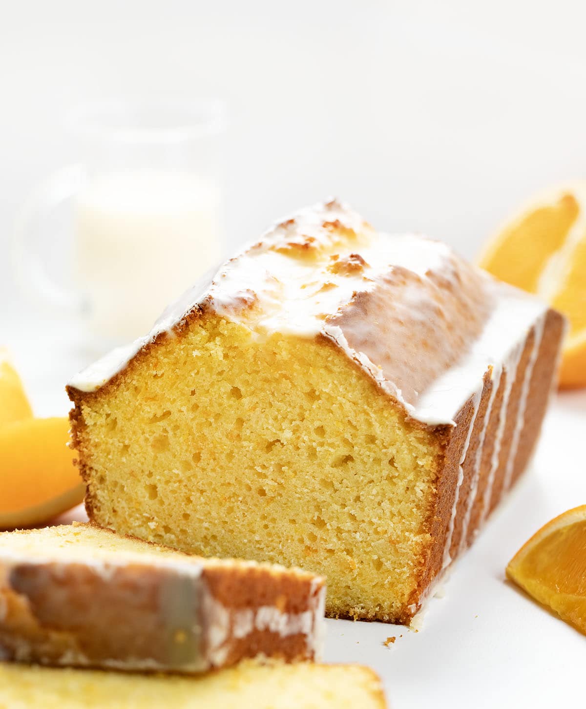 Orange Loaf with some pieces cut away on a white table with fresh oranges.