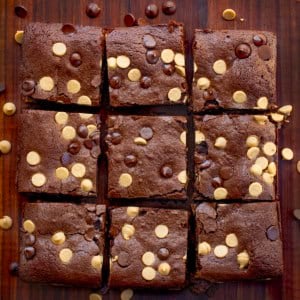 Cut up Peanut Butter Stuffed Brownies on a wooden table with peanut butter chips and chocolate chips.