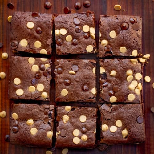 Cut up Peanut Butter Stuffed Brownies on a wooden table with peanut butter chips and chocolate chips.