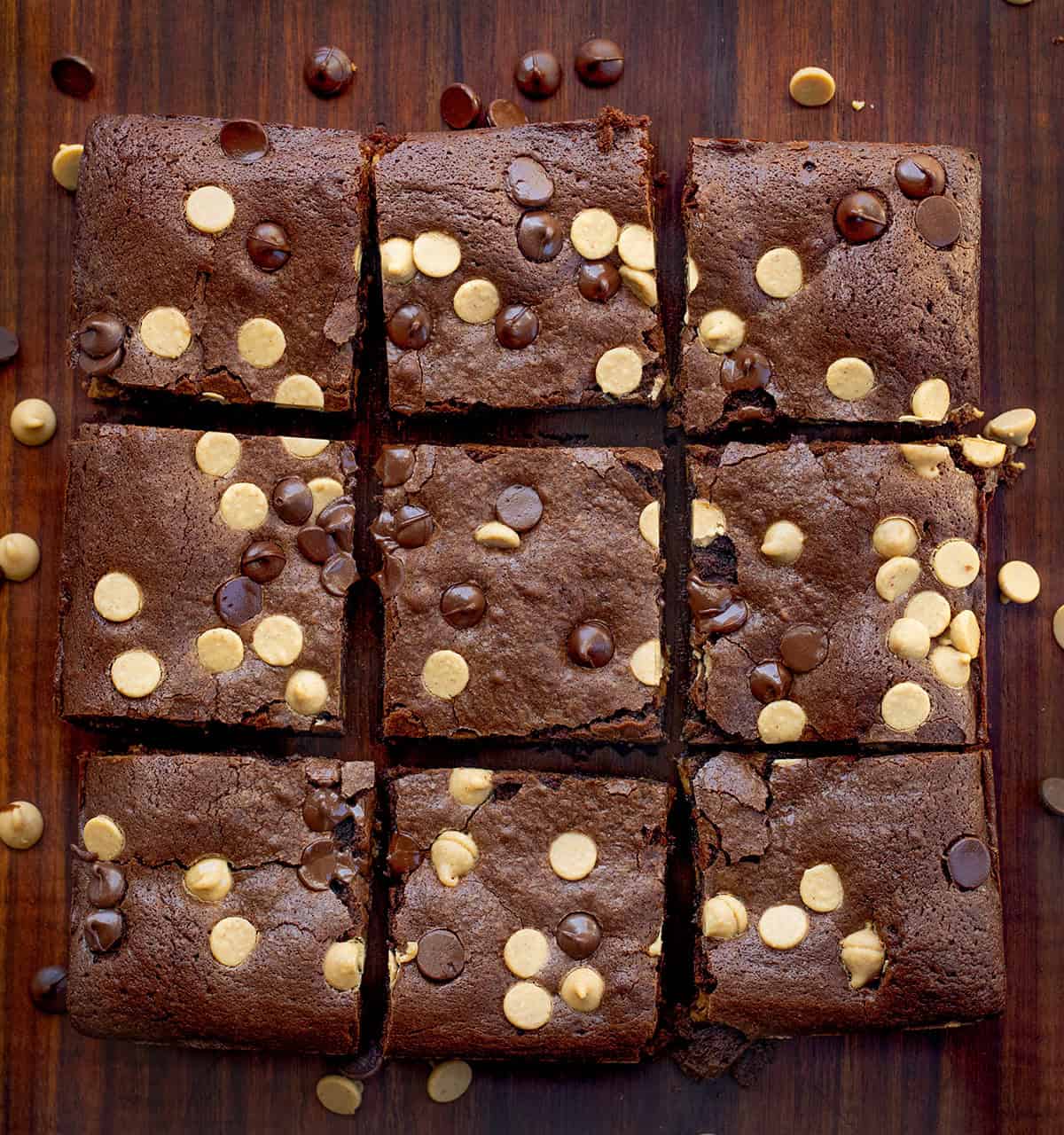 Cut up Peanut Butter Stuffed Brownies on a wooden table with peanut butter chips and chocolate chips.