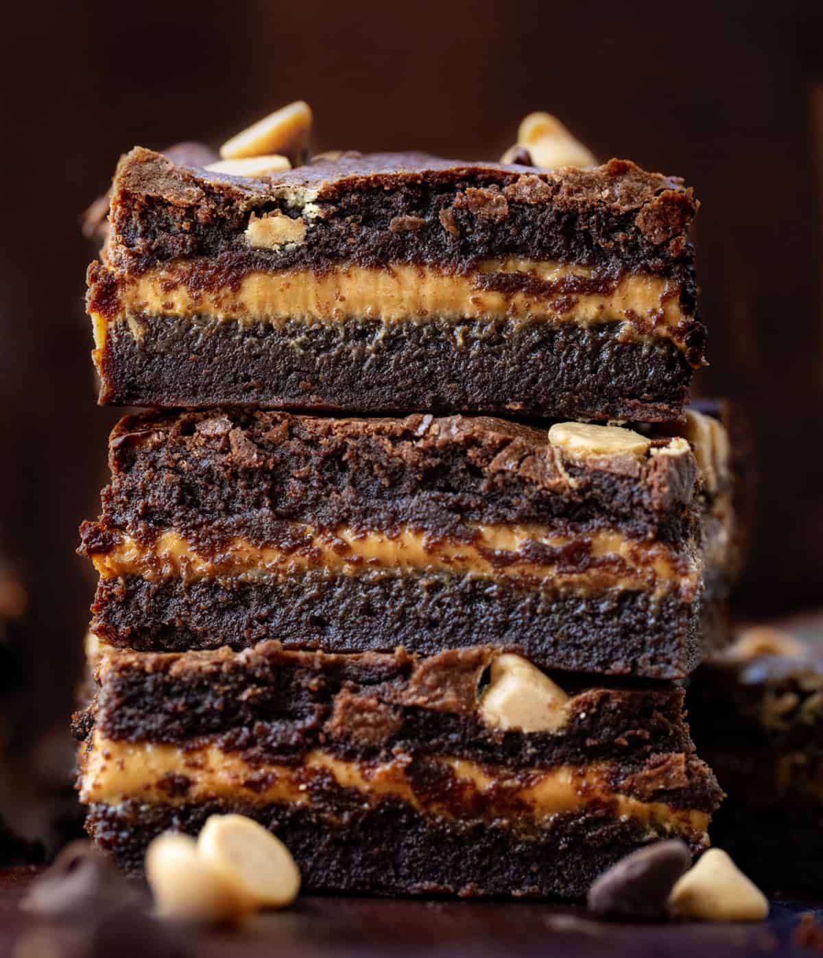 Stack of Peanut Butter Stuffed Brownies on a wooden table surrounded by other brownies.