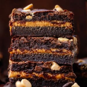 Stack of Peanut Butter Stuffed Brownies on a wooden table surrounded by other brownies.
