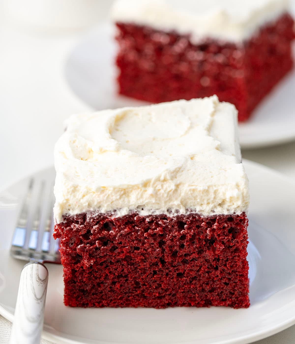 This Easy Red Velvet Sheet Cake delivers all the classic red velvet flavor! Topped with light, silky Ermine frosting, itโs perfect for birthdays, holidays, or just a sweet treat to share! Pieces of Red Velvet Sheet Cake on white plates on a white table.