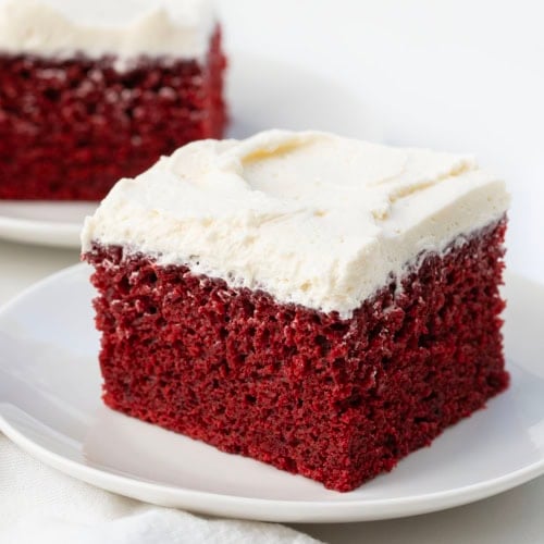 Pieces of Red Velvet Sheet Cake on white plates on a white table.