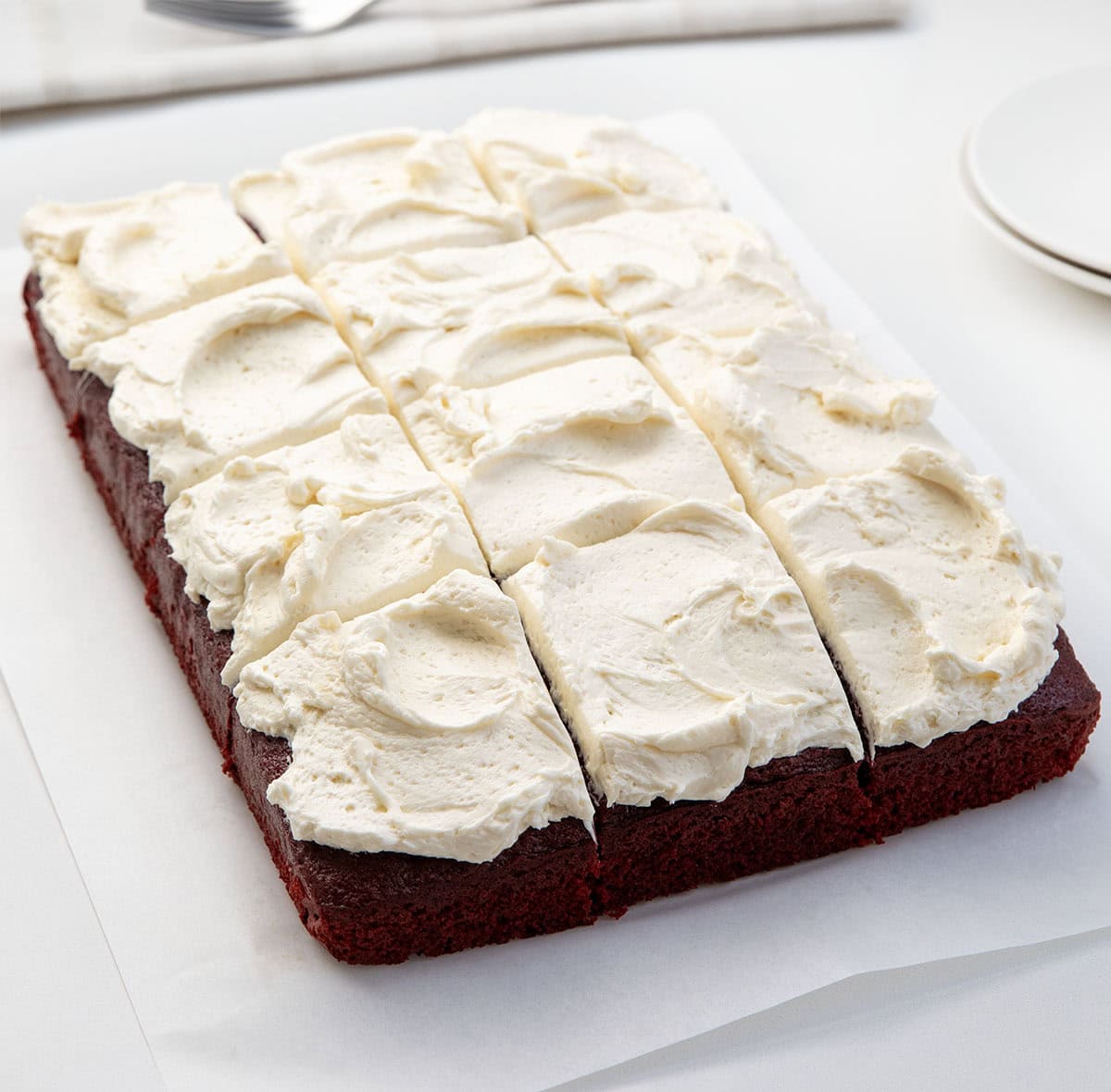 This Easy Red Velvet Sheet Cake delivers all the classic red velvet flavor! Topped with light, silky Ermine frosting, itโs perfect for birthdays, holidays, or just a sweet treat to share! Red Velvet Sheet Cake cut into pieces on a white table.