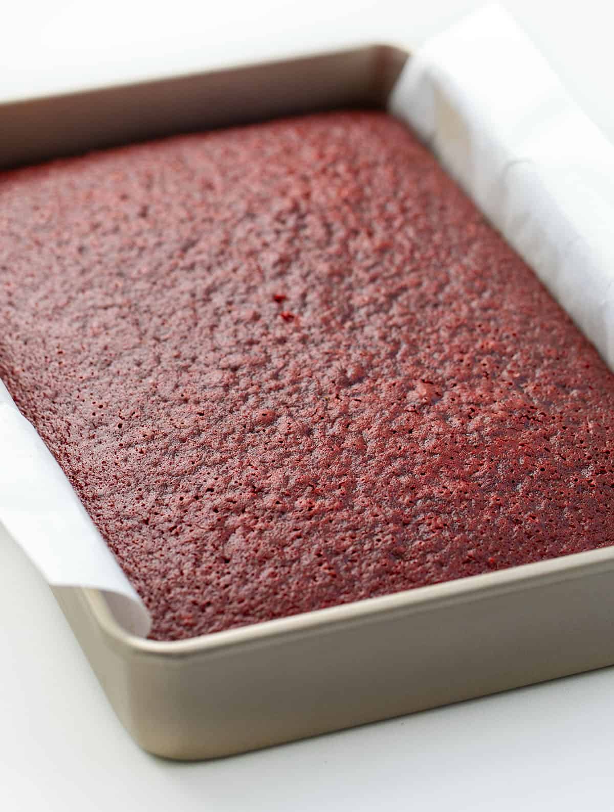 This Easy Red Velvet Sheet Cake delivers all the classic red velvet flavor! Topped with light, silky Ermine frosting, itโs perfect for birthdays, holidays, or just a sweet treat to share! Red Velvet Sheet Cake in a pan on a white table.