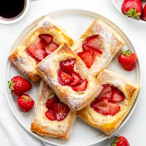 White plate of Strawberry Cream Cheese Danish on a white table with fresh strawberries and fresh coffee.