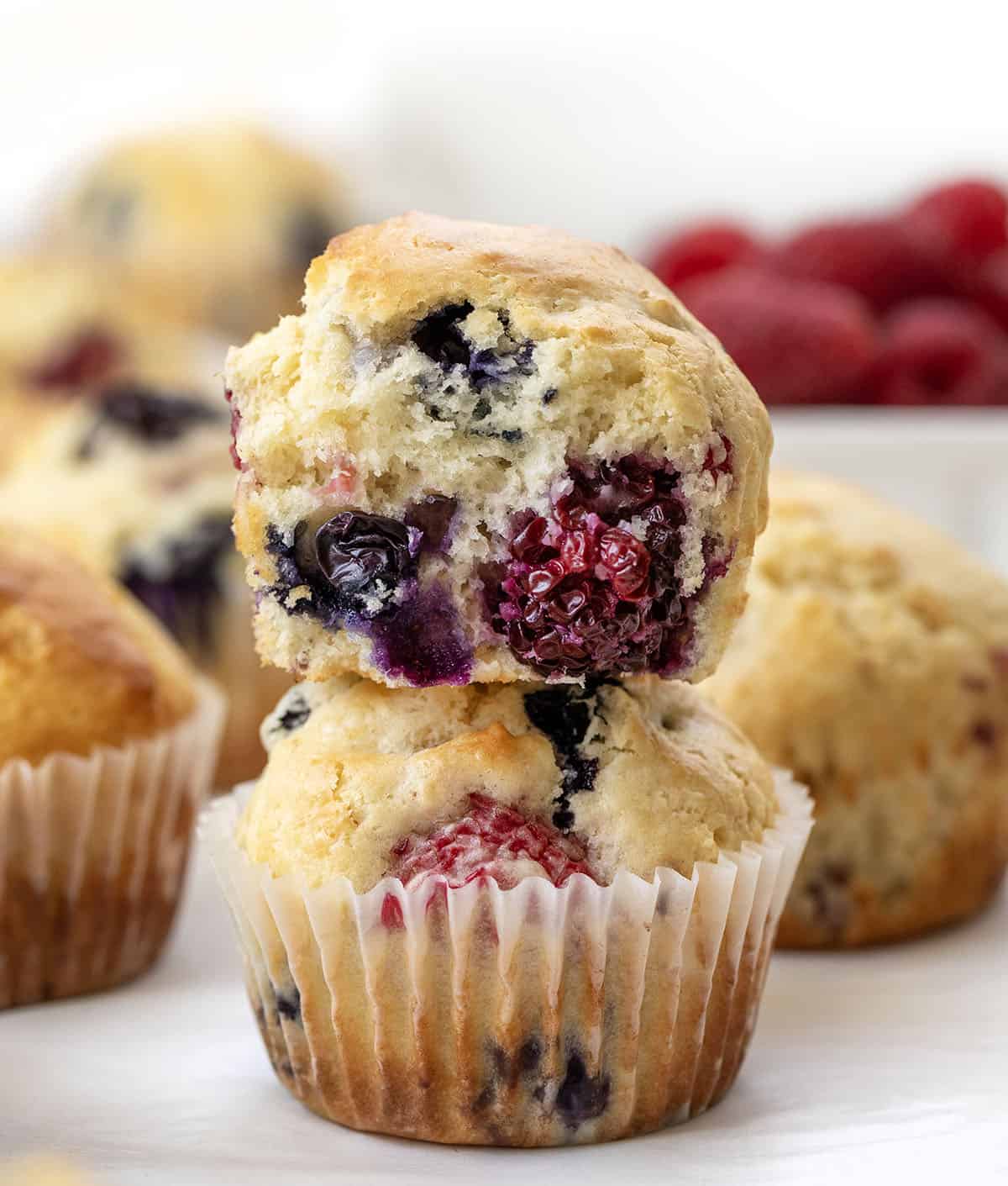 Soft, tender, and filled with a triple threat of flavor, these Triple Berry Muffins are packed with juicy blueberries, raspberries, and blackberries in every bite! Triple Berry Muffins stacked with the top muffin halved, showing the inside texture.