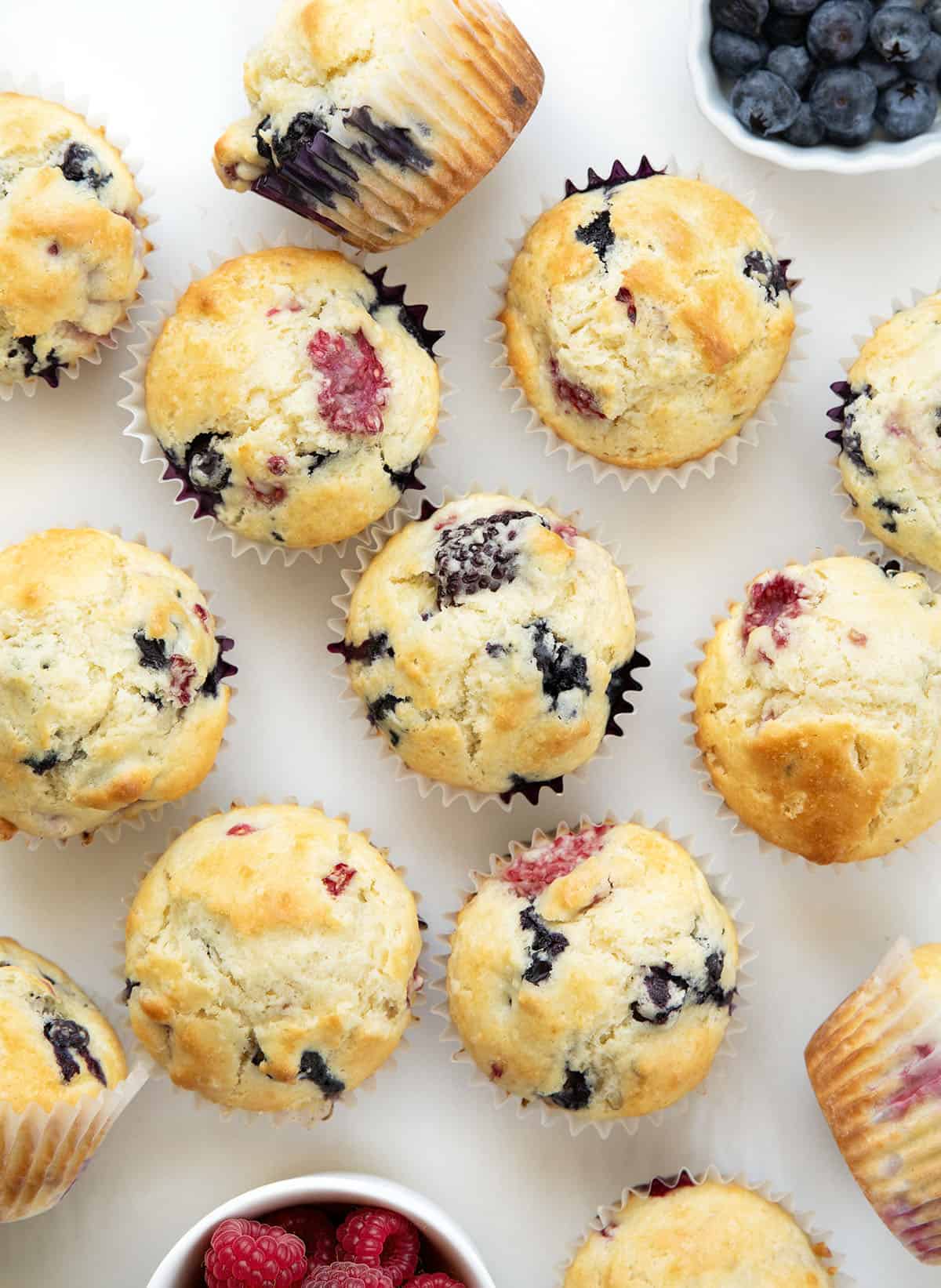 Triple Berry Muffins on a white table with fresh berries from overhead.