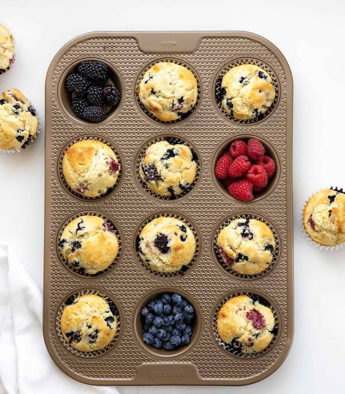 Triple Berry Muffins in a pan with fresh blackberries, raspberries, and blueberries.