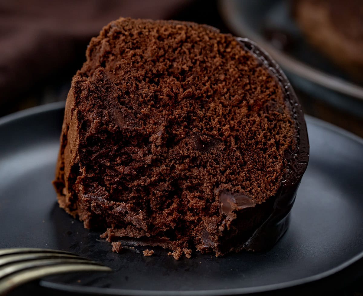 Close up of a piece of Triple Chocolate Pound Cake on its side with a bite taken out and the fork resting on the black plate.